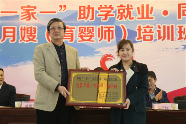 2.湖南中华职业教育社秘书长、湖南温暖工程基金会秘书长杨里平（左）为芙蓉月嫂（育婴师）培训班授班牌
